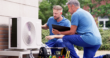 Two hvac technicians assessing unit with clipboard and toolkit nearby