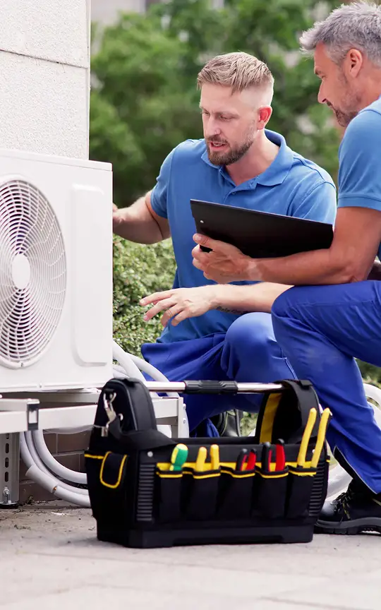 Two hvac technicians assessing unit with clipboard and toolkit nearby